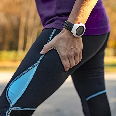 Person standing outdoors holding the upper thigh with one hand, wearing athletic clothing and a wristwatch.